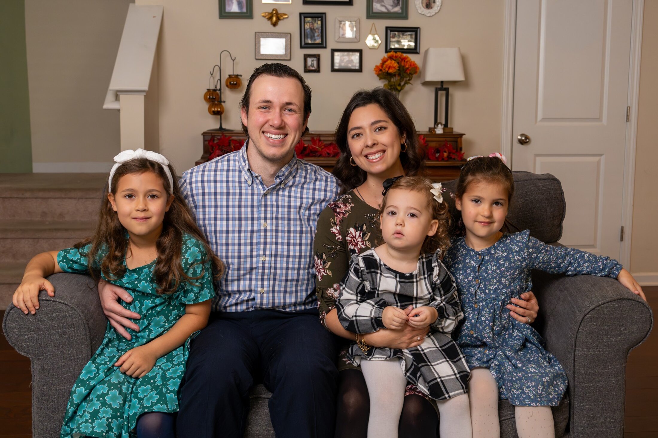 A young couple sits on the couch with their three little girls.
