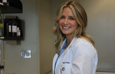 Headshot of smiling blonde woman wearing a white lab coat.