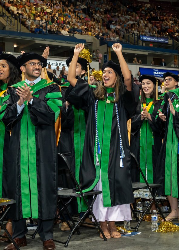Graduates wearing green and black robes and caps celebrate their commencement ceremony.
