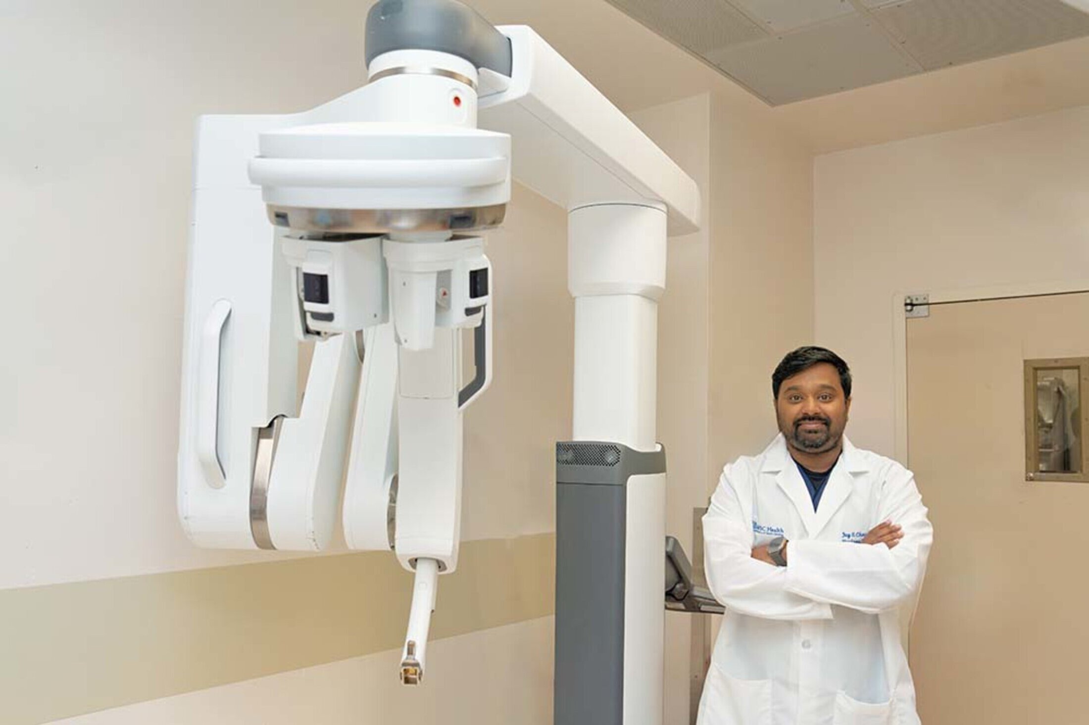 Doctor in white coat stands in front of a machine in a surgical suite.
