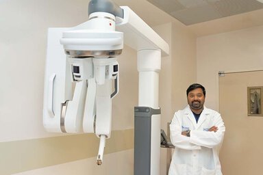 Doctor in white coat stands in front of a machine in a surgical suite.