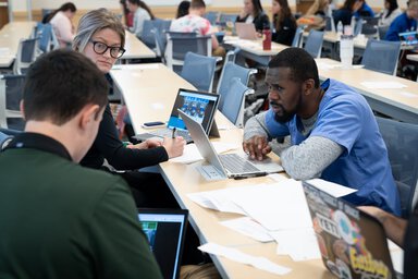 Three students working together on laptops at long tables in an MUSC classroom