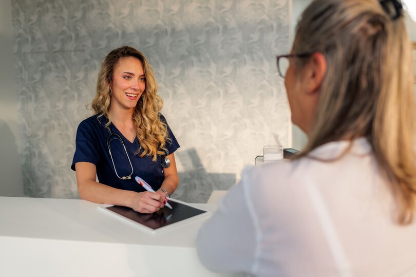 Friendly female doctor engaging with a patient while using a tablet at the hospital reception desk, offering medical assistance and support in a welcoming environment