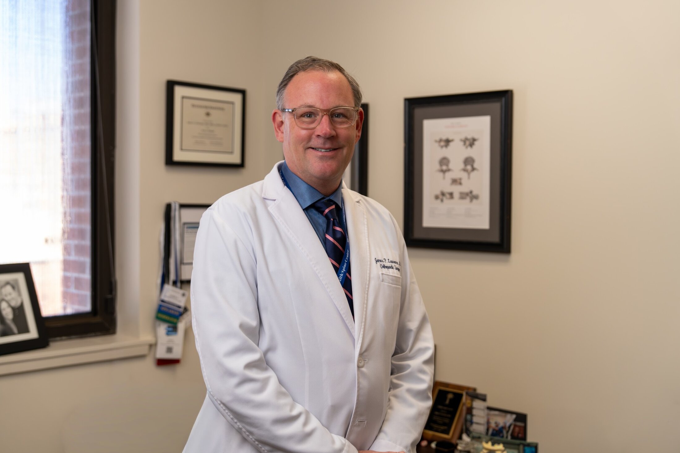 A physician poses in his office surrounded by career mementoes.