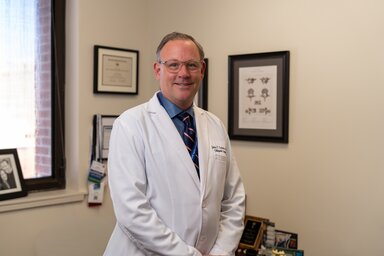 A physician poses in his office surrounded by career mementoes.