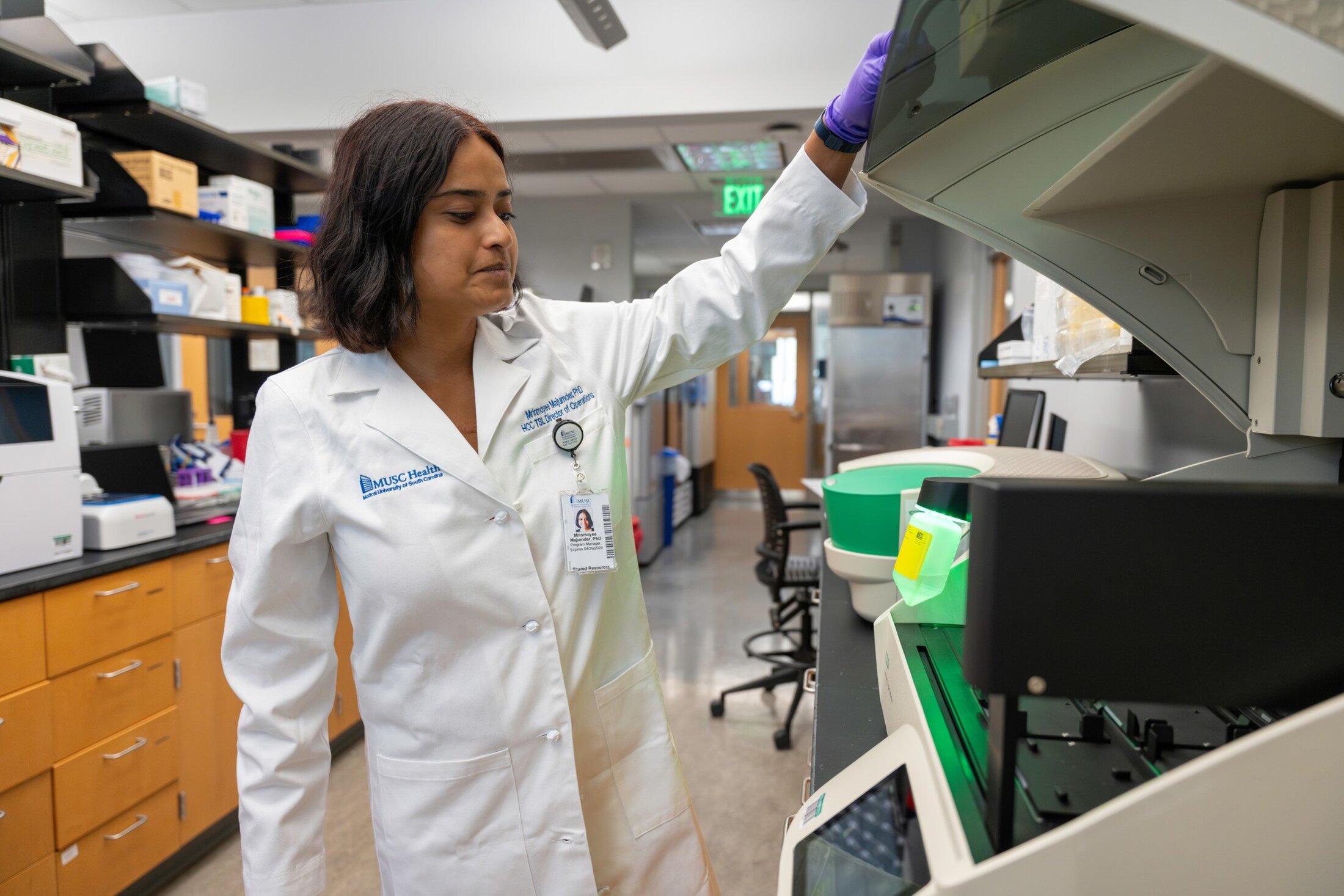 A woman in a white lab coat opens a machine in a cancer research lab.