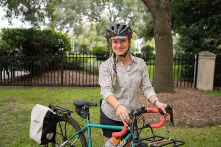 a woman in a bike helmet stands holding her bike
