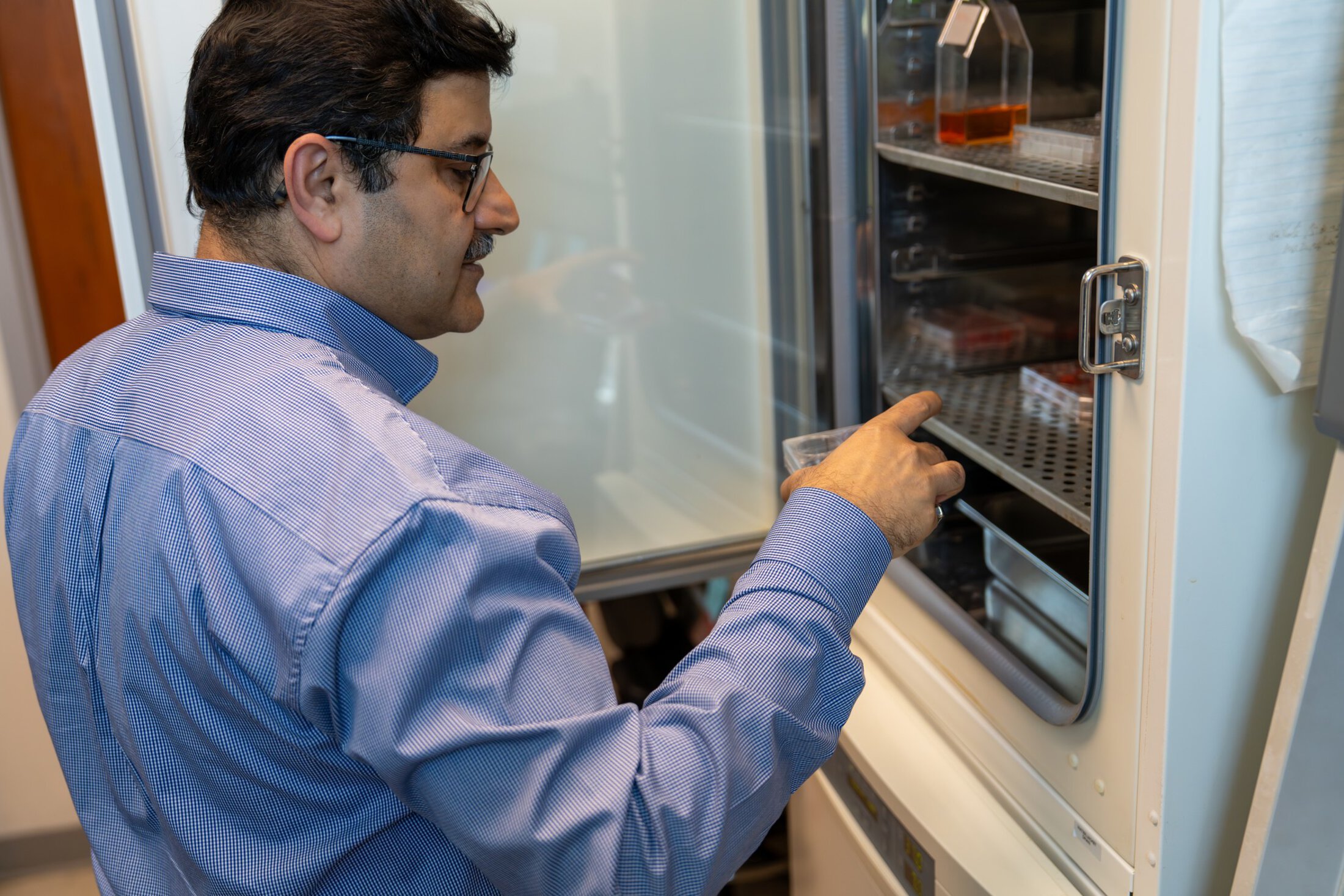 A researcher regards a sample as he removes it from a refrigerator.