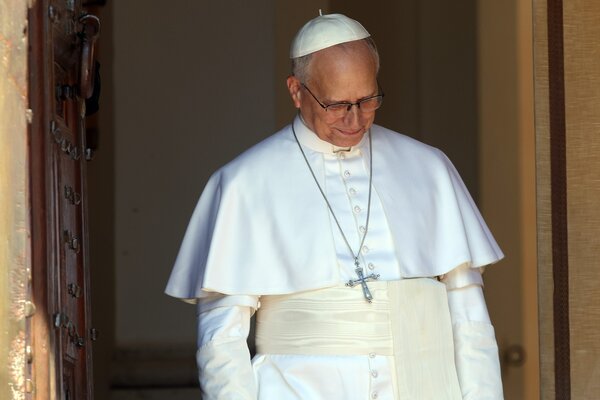 The pope in white robes glances down as he stands in a doorway.