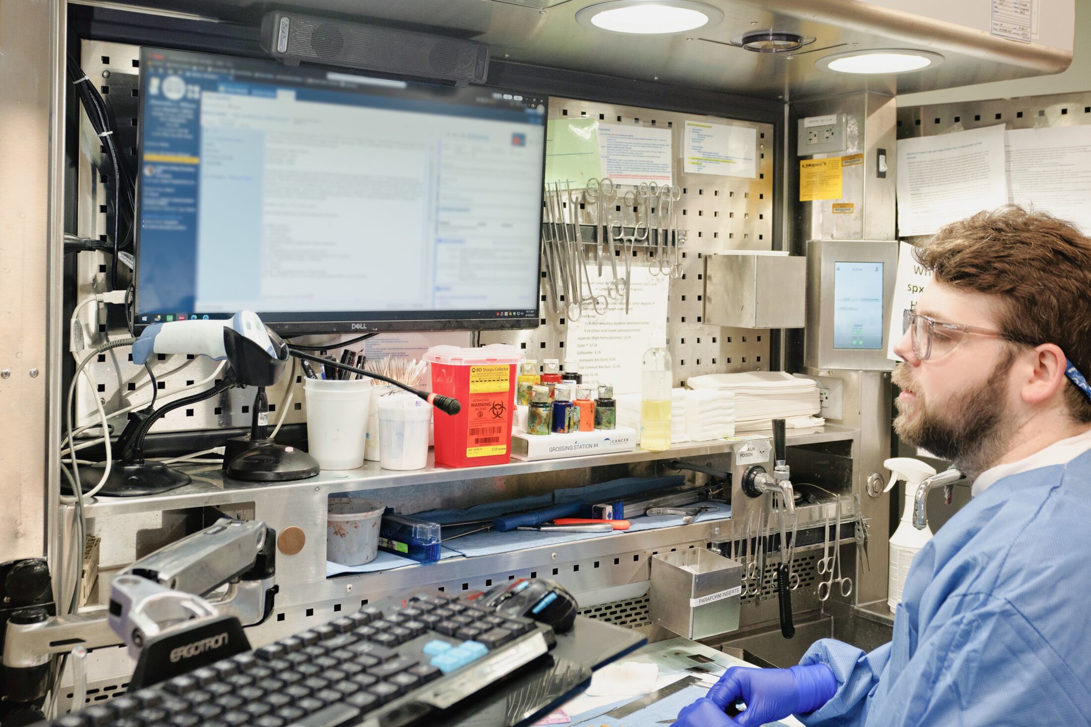 A man in blue scrubs works in a lab with a tissue sample.