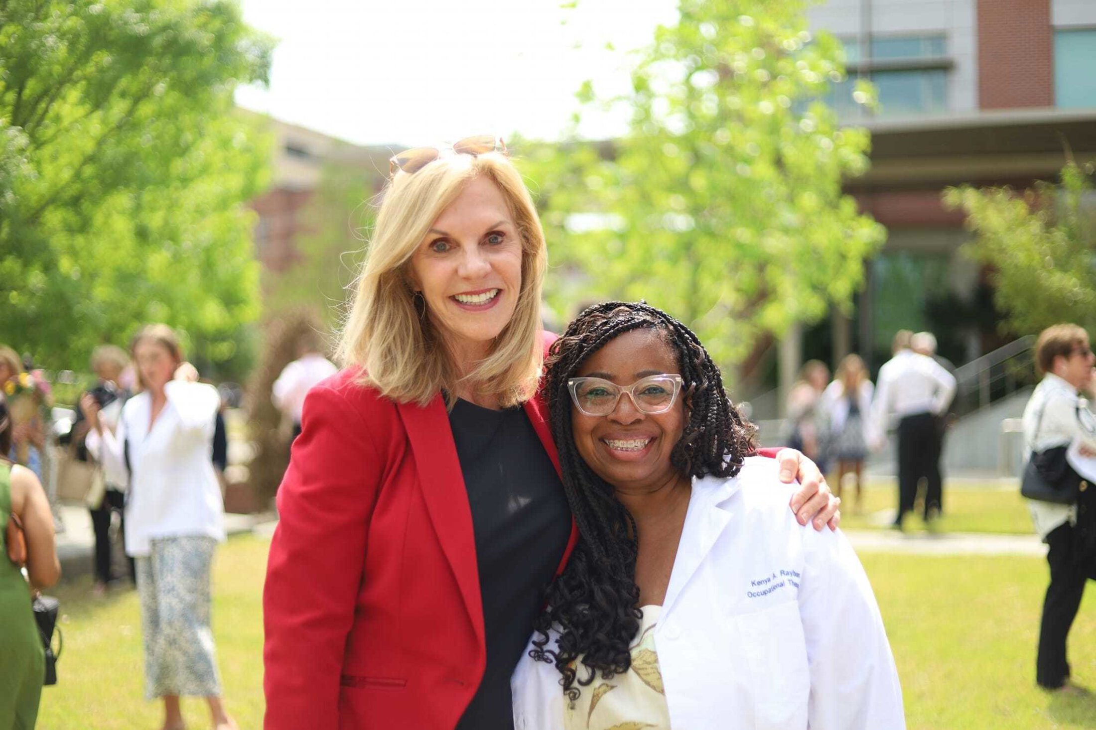 A woman in red jacket and woman in white coat stand together and pose.