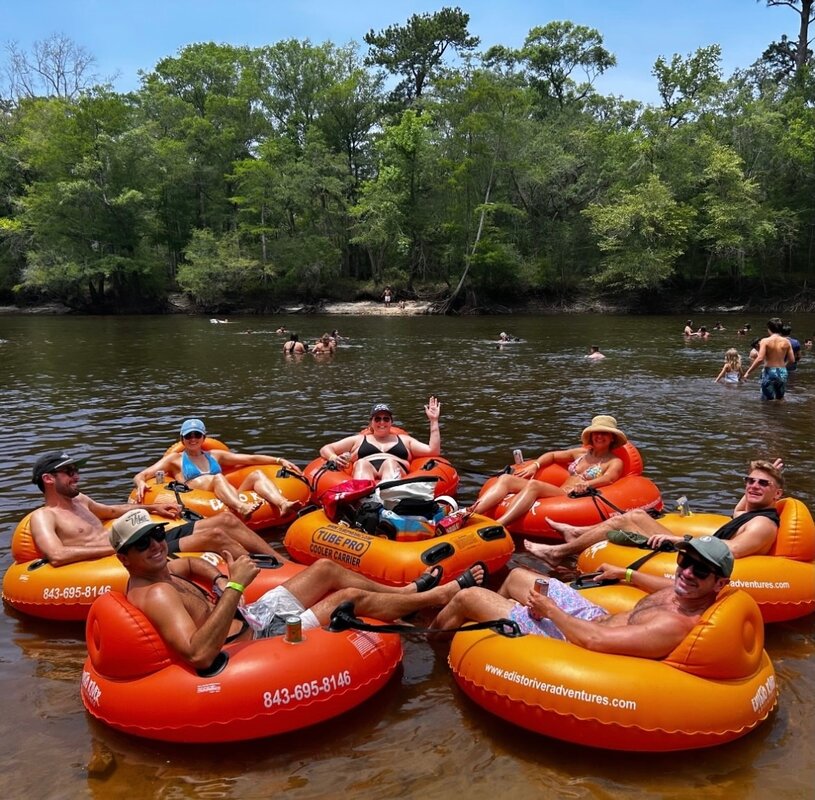 6 adults in orange innertubes on a river
