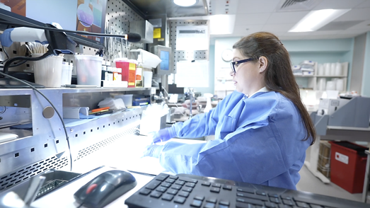 A woman wearing blue scrubs handles samples in a pathology lab.