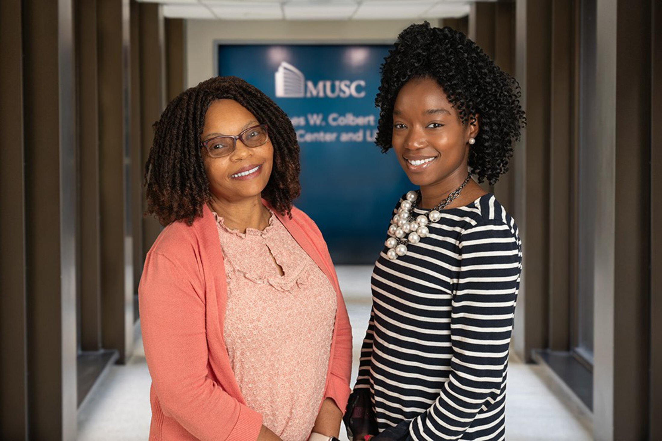 Two women pose in a hall leading to the MUSC library.