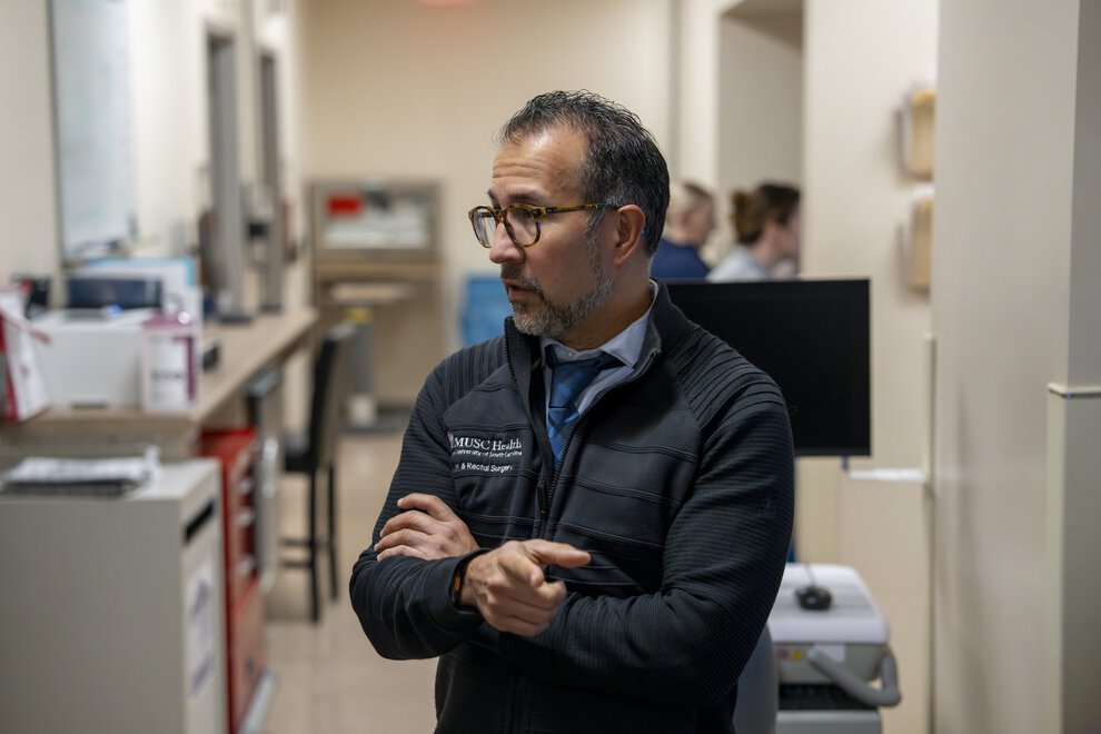 A doctor in a clinic work area gestures as he talks to someone off screen.