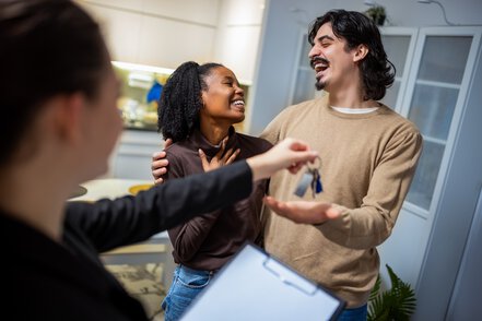 Real estate agent smiling while handing apartment keys to a mixed couple, symbolizing a successful move and new beginning.